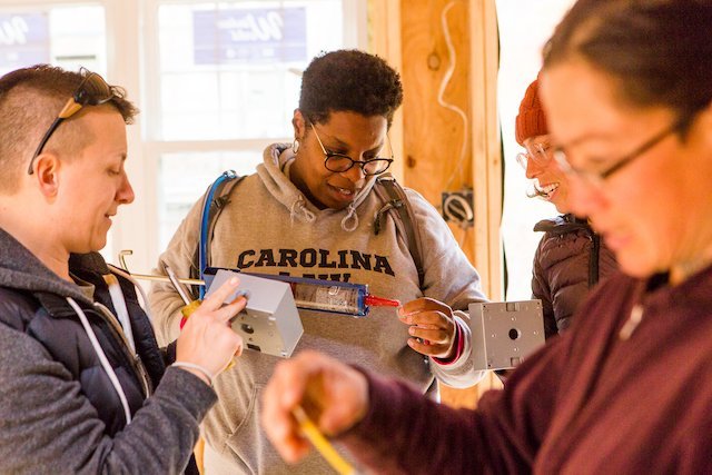 Four students work together with electrical box during building apprenticeship.