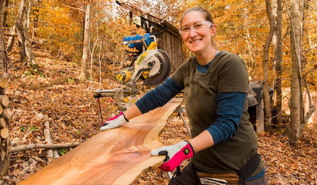 Student smiles while carrying rough cut lumber during building apprenticeship