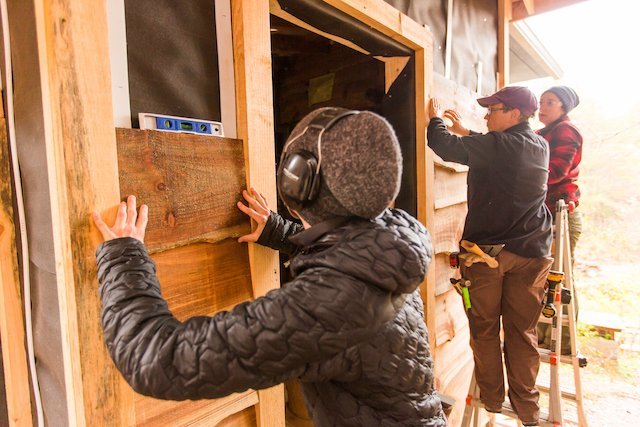 Building apprenticeship students install wood siding on house.