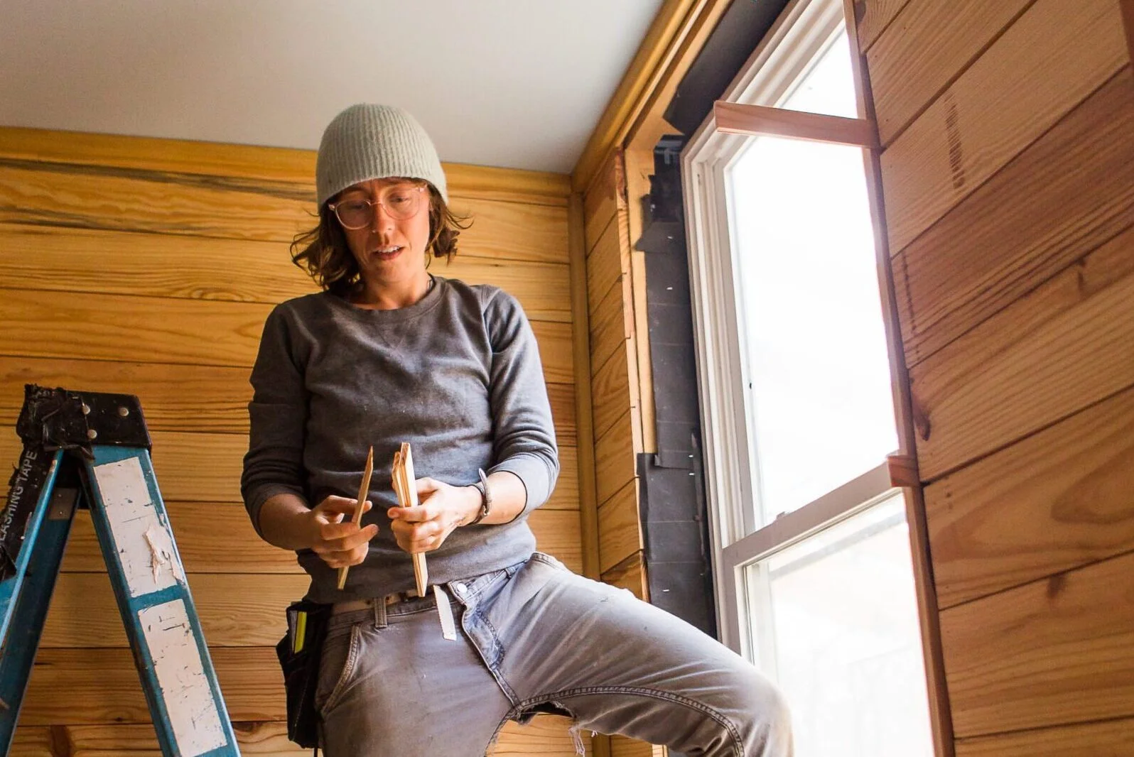 woman installing a salvaged window while building a tiny house