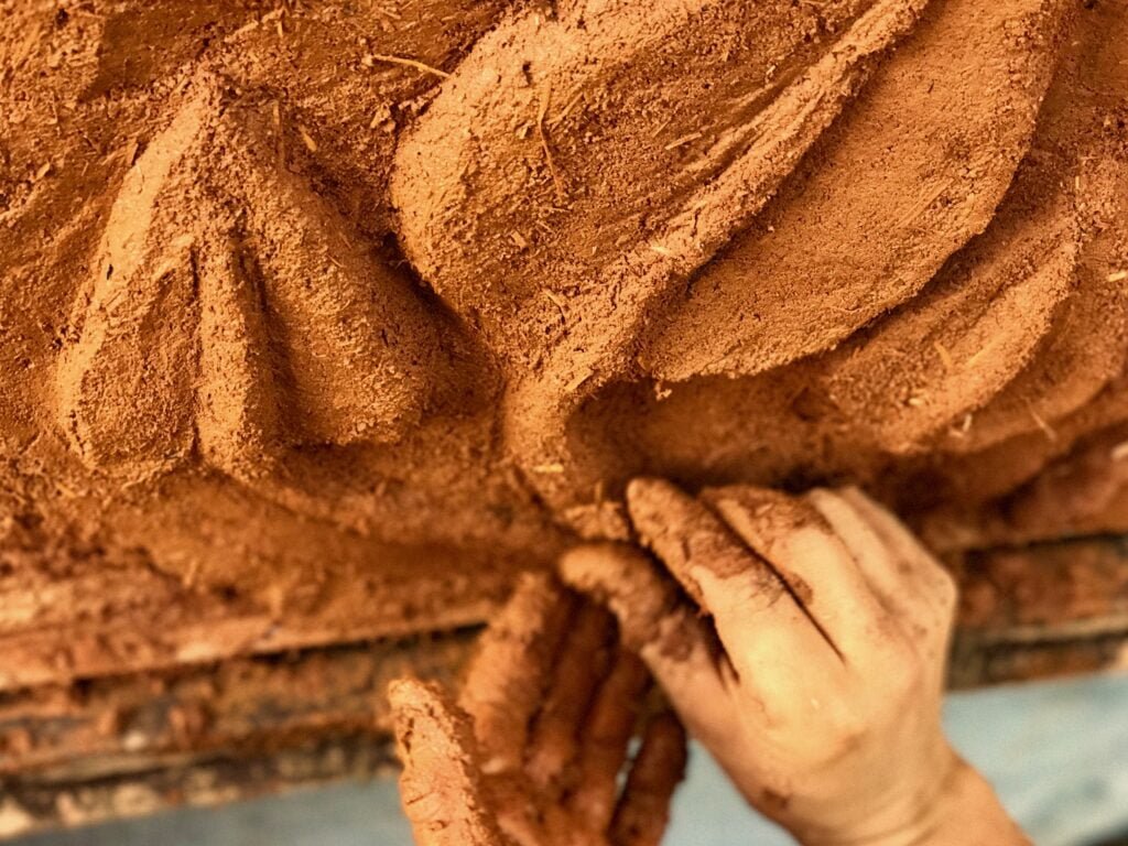 Closeup of hands sculpting cob on a structure