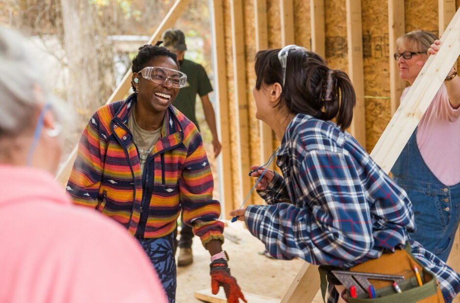 Older women students watch as 2 young women students laugh and smile during a tiny house building workshop at wild abundance