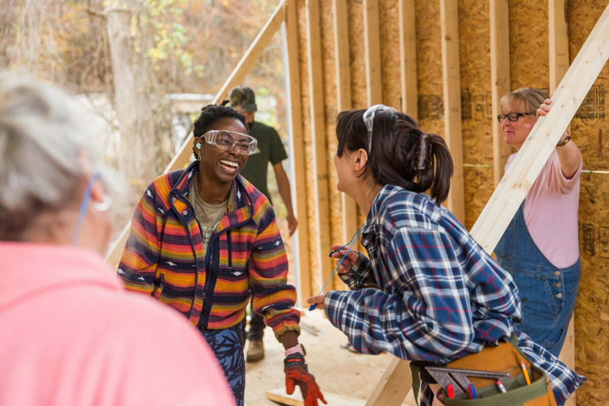 006-Tiny House Workshop-Fall 2023-WildAbundance (2) Older women students watch as 2 young women students laugh and smile during a tiny house building workshop at wild abundance