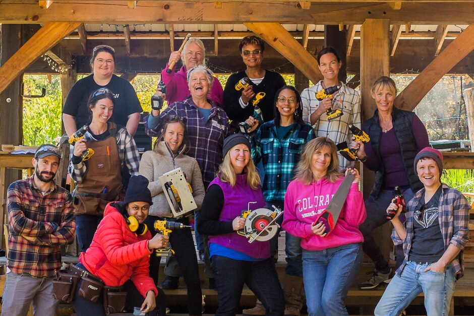 Women's Basic Carpentry Class posing for a group picture with everyone holding up a tool and smiling
