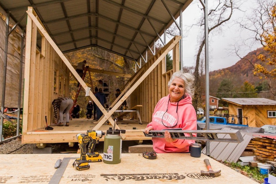 An older woman smiles up from a work table where she's gotten a level to use in a tiny house building workshop