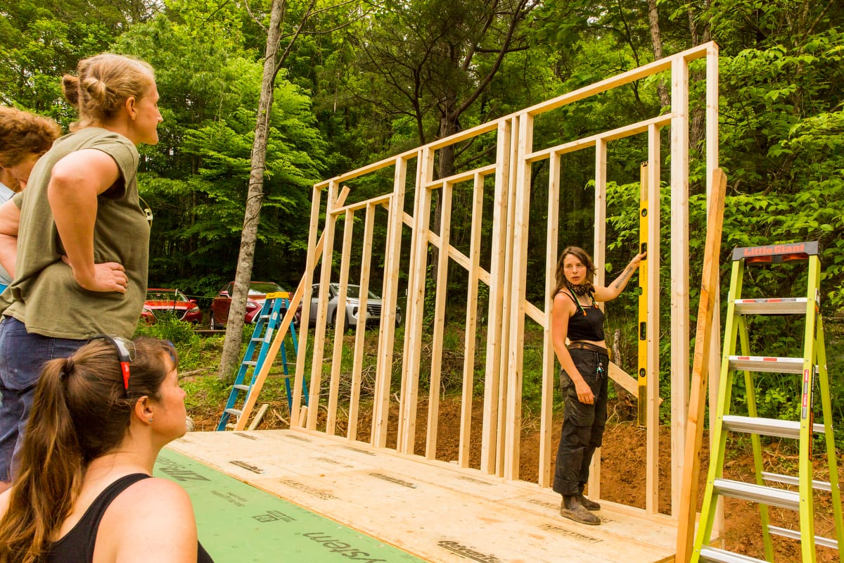 014_WAC-bathhouse PFC campus development-wall raising-Nadi-spring2025-©SarahTew An instructor teaches students structural building techniques after raising the first wall of their build during a Women's Advanced Carpentry workshop at Wild Abundance in North Carolina