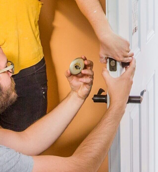 Two students in a hands-on building and carpentry program learning how to install a door handle and lock