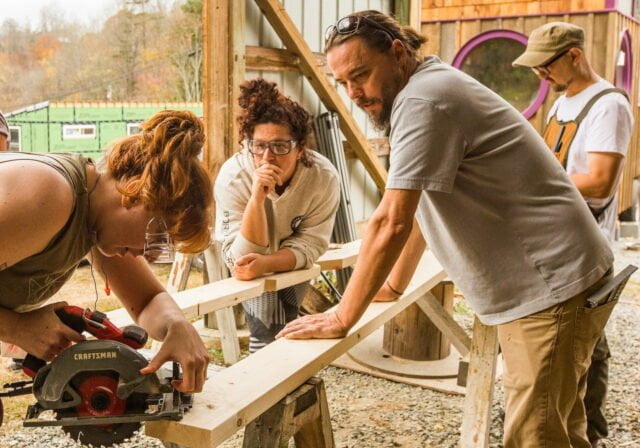 Jeremy instructs a woman in the Tiny House Building Workshop as she attempts a tricky cut with a circular saw