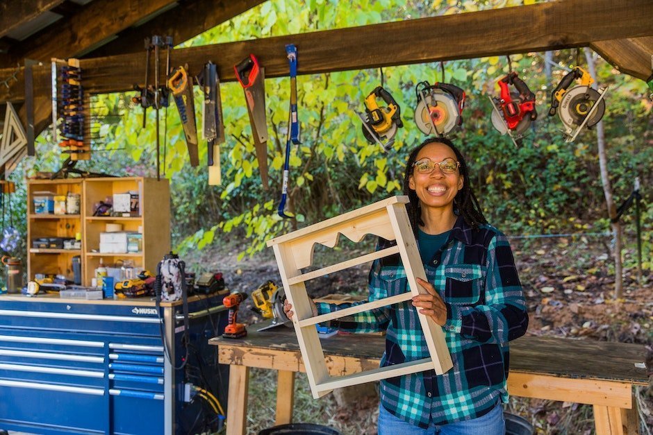 Black woman holding up a small bookshelf she made in the outdoor wood shop at Wild Abundance