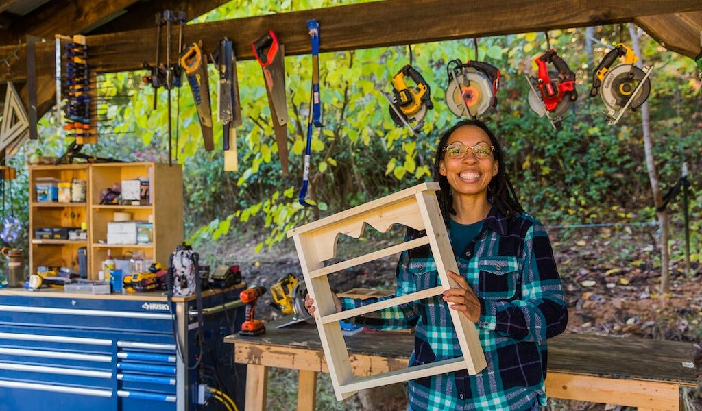 woman holding up a small bookshelf she made in the outdoor wood shop at Wild Abundance
