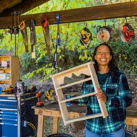 woman holding up a small bookshelf she made in the outdoor wood shop at Wild Abundance
