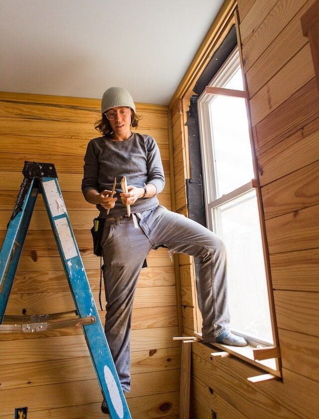student installing interior trim around a window in a room with rustic wood paneling