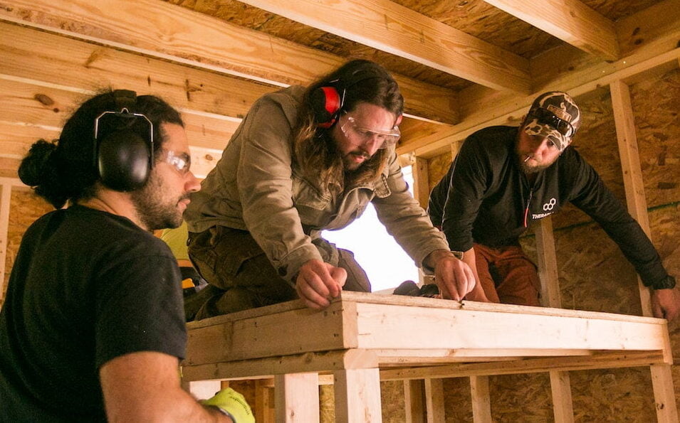3 young men work together to build the loft for a bed inside a tiny house