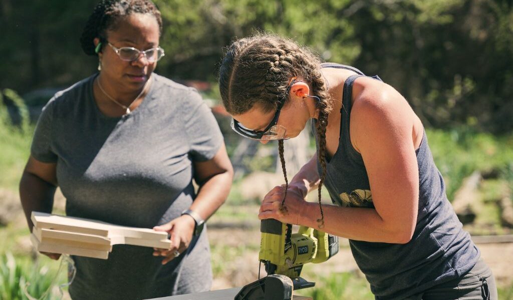Two women work together to use a jigsaw to cut a board during a women's basic carpentry course at Wild Abundance