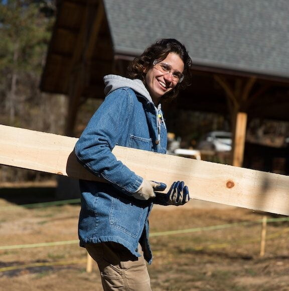 A young female student carrying lumber to a building project in a carpentry class