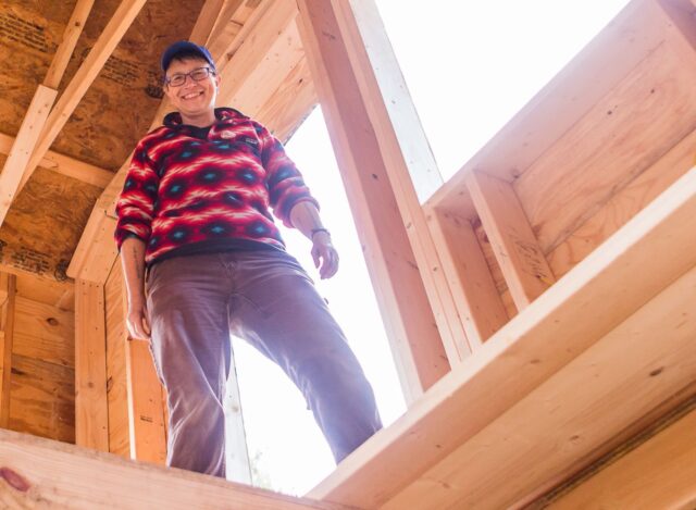 A female smiles proudly in a building she's been working on constructing with a carpentry class