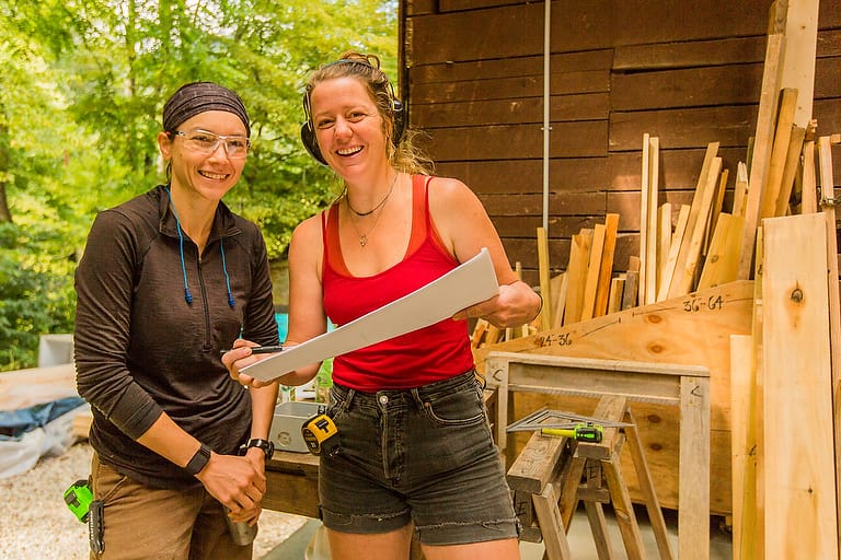 A female instructor and a student look at building plans for a structure they are constructing with a women's advanced carpentry class at Wild Abundance in North Carolina