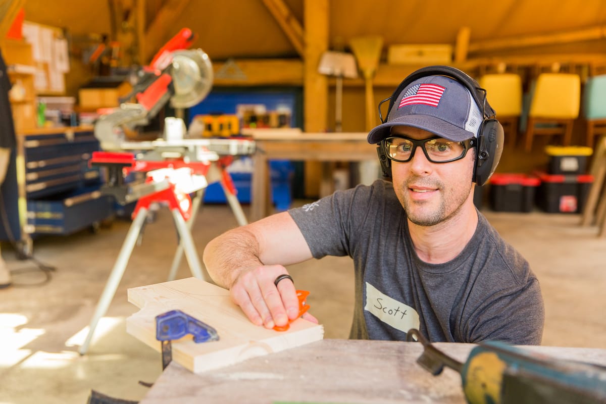 ABC-1200-2025-100 A male student smiles up from working on his personal project on the last day of an introductory carpentry workshop at Wild Abundance in North Carolina
