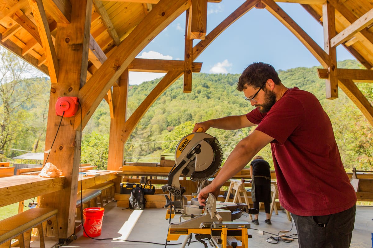 ABC-1200-2025-103 A student practices using a mitre saw as they build their personal project on the final day of a 4 day adult beginner carpentry workshop at Wild Abundance in North Carolina