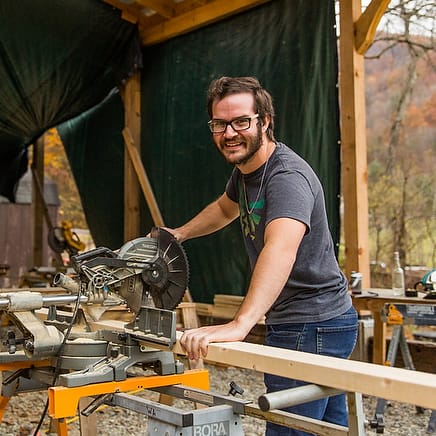 A male student practices cutting wood at a mitre saw during an adult beginners carpentry workshop intensive at Wild Abundance