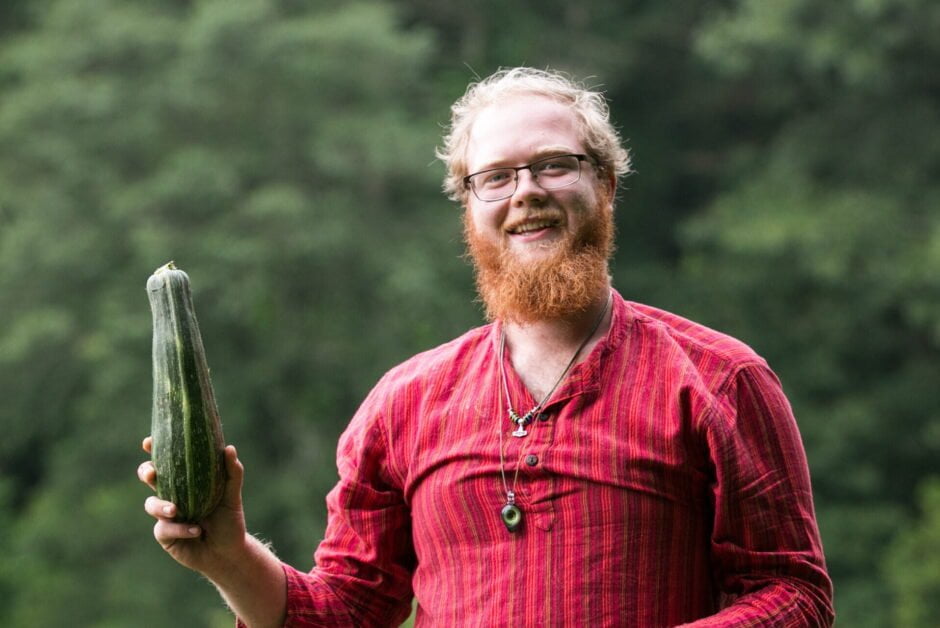 Man standing in a garden holding a squash he grew and harvested