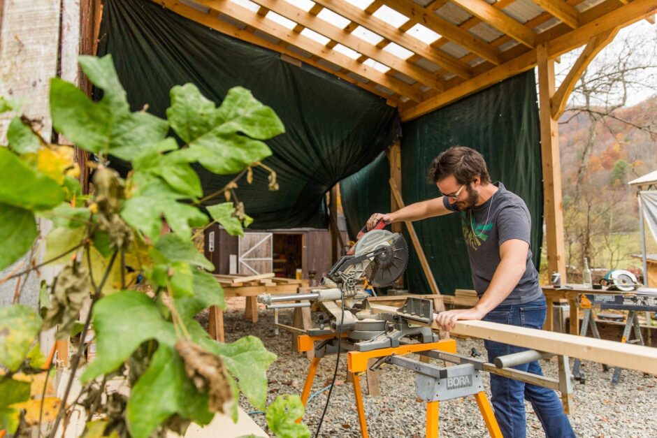 A male student uses a mitre saw to practice making cuts in wood boards during an all genders basic woodworking class