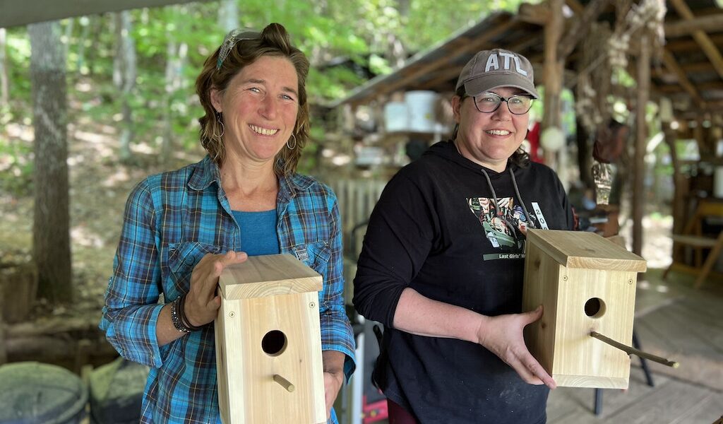 Two women smile while showing off a birdhouse one of them made during a women's woodworking program