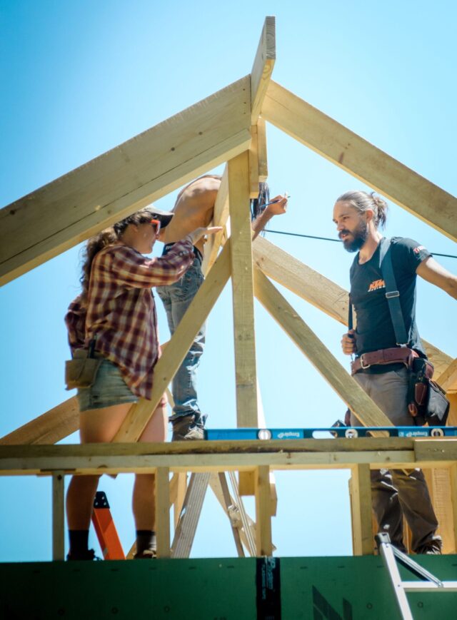 Natalie and Austin standing at the peak of a roof during construction of infrastructure for the Wild Abundance campus