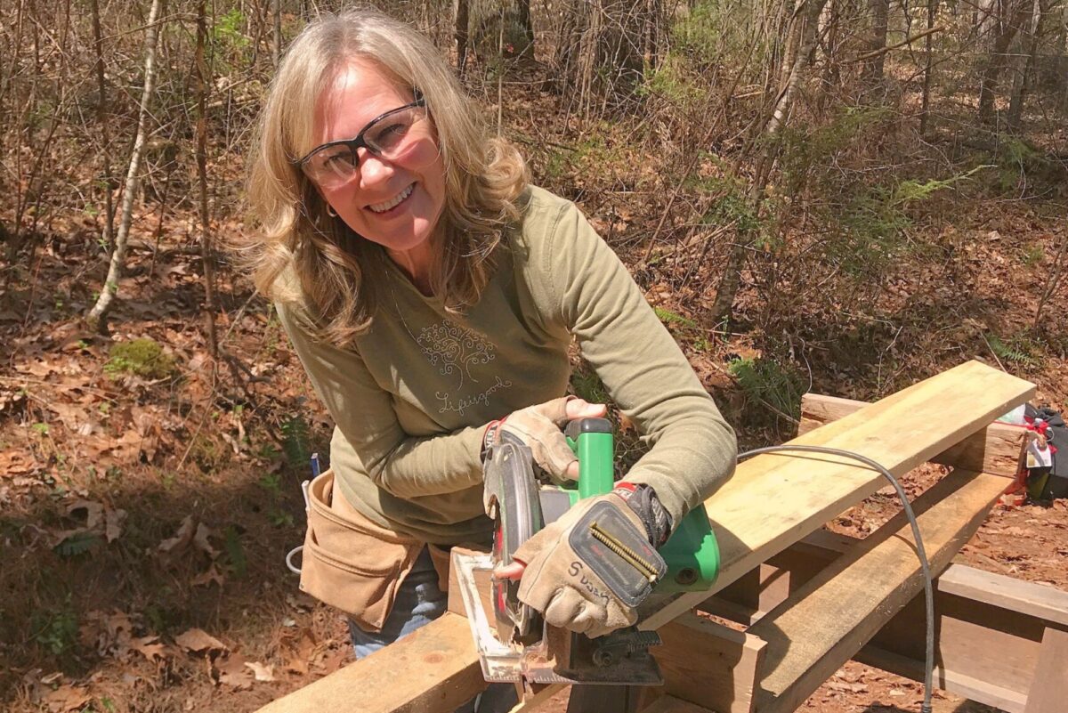 middle aged woman using saw nature background Older woman learning carpentry in a class at Wild Abundance