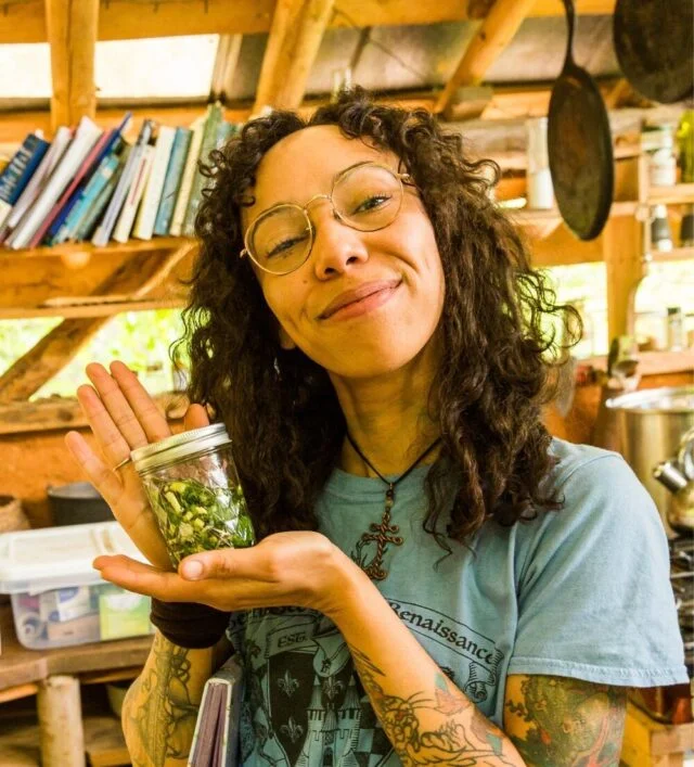 a student smiles holding a jar of tincture she's prepared using medicinal herbs foraged and processed during a wildcrafted apothecary course at wild abundance