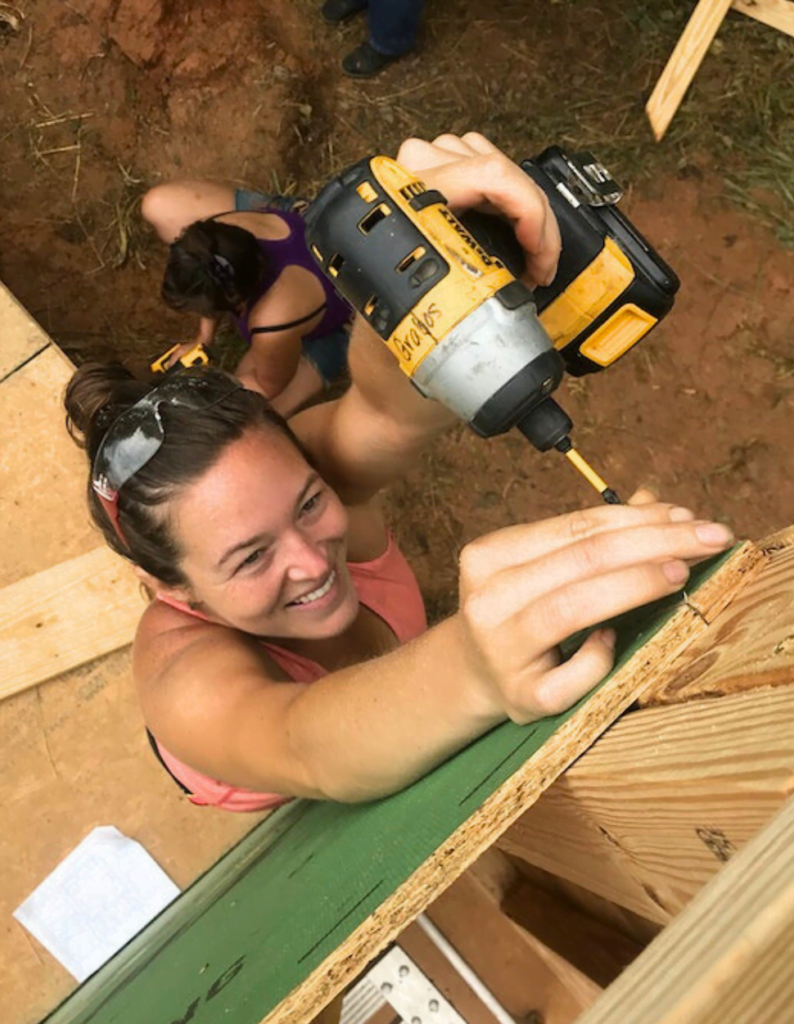 white woman uses an impact driver to attach a board 