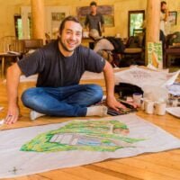 A male student smiles up from his permaculture design project drawings for a PDC class