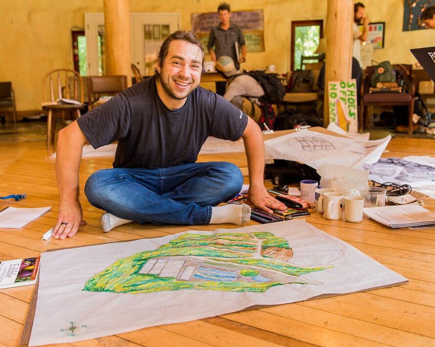 A male student smiles up from his permaculture design project drawings for a PDC class
