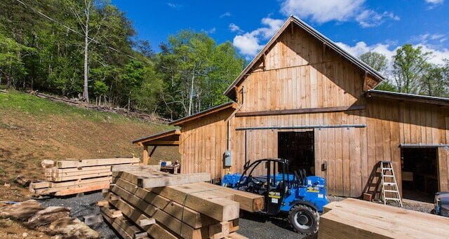 The exterior of Ivy Creek Timber Framing Workshop with a pile of stacked beams