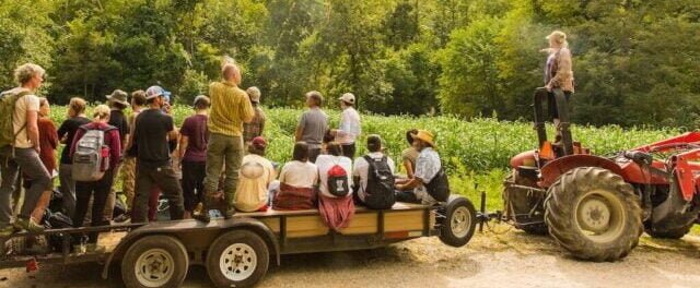 A PDC class riding on a tractor-pulled trailer is getting a tour of the permaculture landscaping and farm fields at Earthaven Ecovillage.