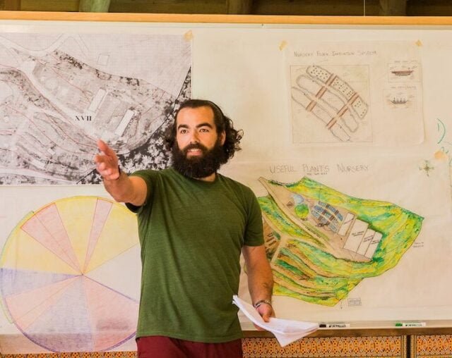 A student speaks in front of his group's permaculture design drawings during a presentation at the end of the course