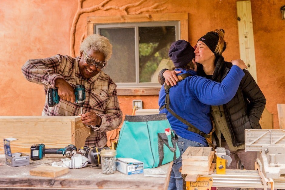 An older woman works on her carpentry class project while 2 other students hug goodbye on the last day of basic carpentry class at Wild Abundance's campus