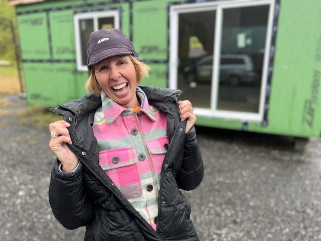 A woman student smilies, holding her puffy coat open to show a flannel shirt layer beneath it: she's prepared for all weather conditions