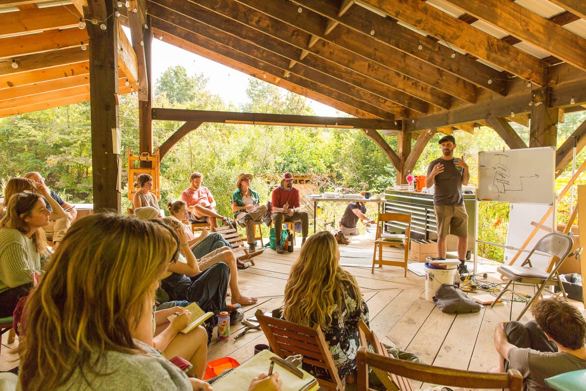A permaculture design student's hands are shown drawing intricate landscape plans with  plant labels and coloring as they prepare their final project to earn their permaculture design certificate at the annual Wild Abundance PDC