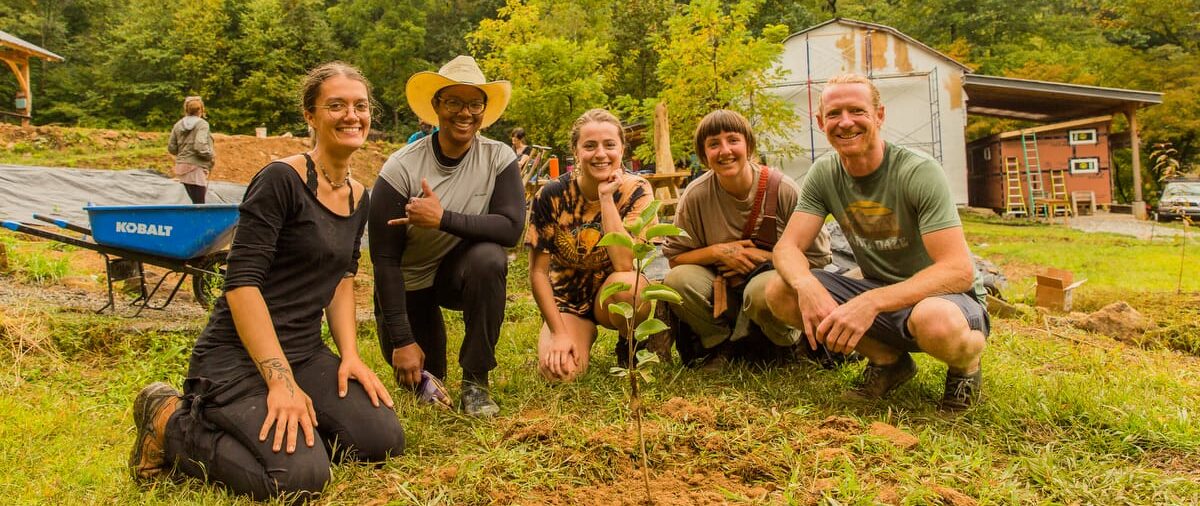Permaculture Students smile in front of a pear tree they just planted in an experiential learning session during the annual PDC or Permaculture Design Certificate Course at Wild Abundance in North Carolina