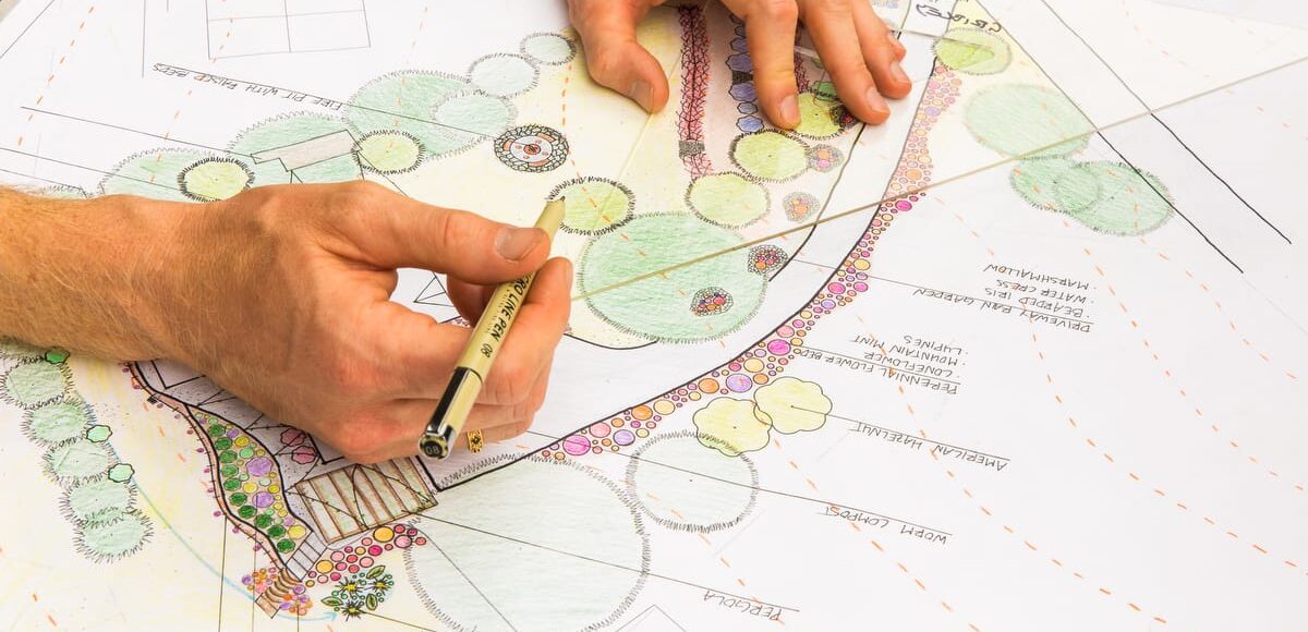 PDC-1200-2025-113 A permaculture design student's hands are shown drawing intricate landscape plans with plant labels and coloring as they prepare their final project to earn their permaculture design certificate at the annual Wild Abundance PDC