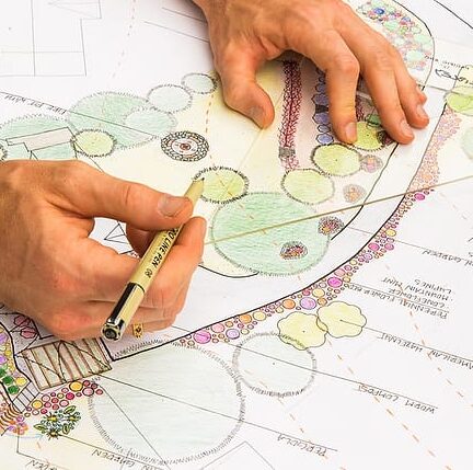 A permaculture design student's hands are shown drawing intricate landscape plans with plant labels and coloring as they prepare their final project to earn their permaculture design certificate at the annual Wild Abundance PDC