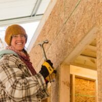 A young woman student smiles down from a ladder where she is working on building a tiny house during a workshop at Wild Abundance.