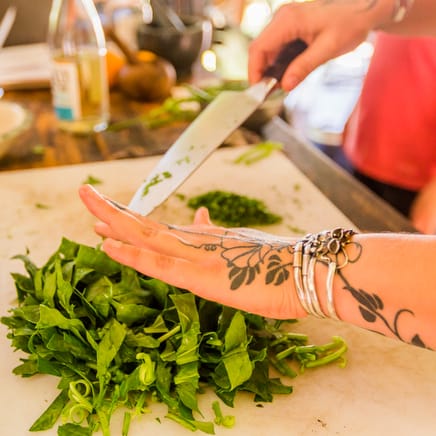 A student chopping vegetables for a recipe under an instructor's guidance in a cooking class at the Nourishing Foods retreat for women at Wild Abundance