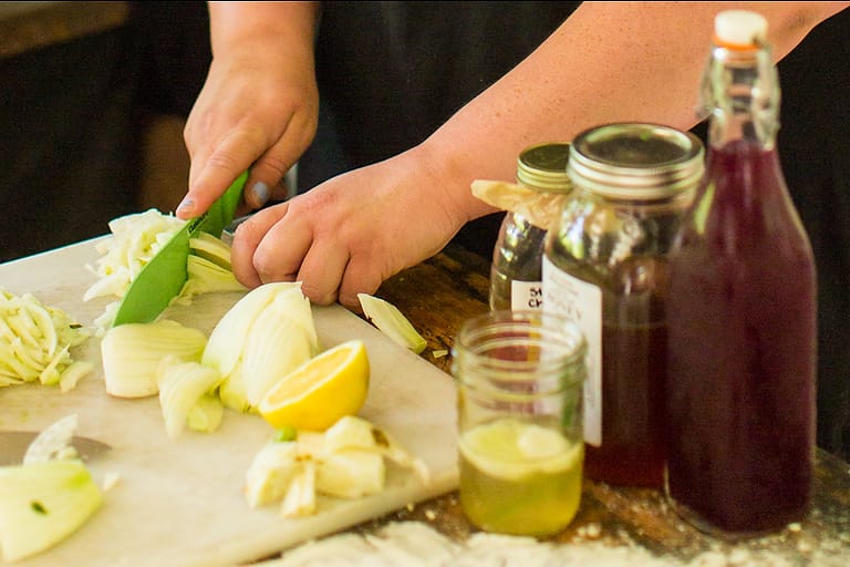 A student chopping vegetables for a recipe under an instructor's guidance in a cooking class at the Nourishing Foods retreat for women at Wild Abundance