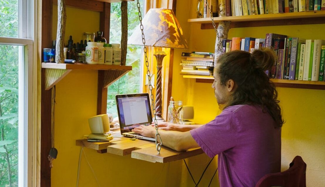 P1022876-fold out desk for laptop in tiny home A person works on their laptop at a small fold-down desk built to save space when not in use inside of a tiny home