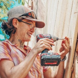 Woman using an impact driver to attach siding to a tiny house in a workshop at Wild Abundance