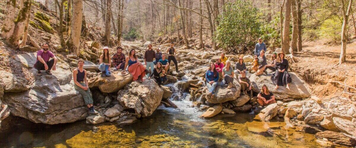 001_Instructor Group Wild Abundance 2025-©SarahTew (1) Wild Abundance staff and instructors standing over a waterfall in a forest in the blue ridge mountains for a group picture