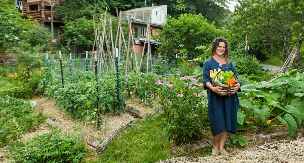 STew-5412-Natalie portrait basket harvest vegetables summer-1340-WA-Gardening Book-SarahTew2024-Natalie basket harvest garden land based living Natalie Bogwalker, author of the Wild Abundance Guide to Land-based living, poses for a photo with a basket of freshly harvested vegetables in front of her garden and homestead in Western North Carolina