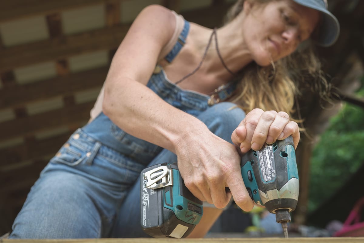 55-HandyHomeownerBootcamp-WildAbundance A woman using an impact driver to repair a deck after taking DIY skills classes at Wild Abundance
